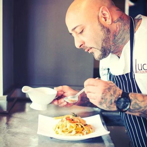 chef antonio (tony) caruana with tattoos is eating a plate of food with a spoon .