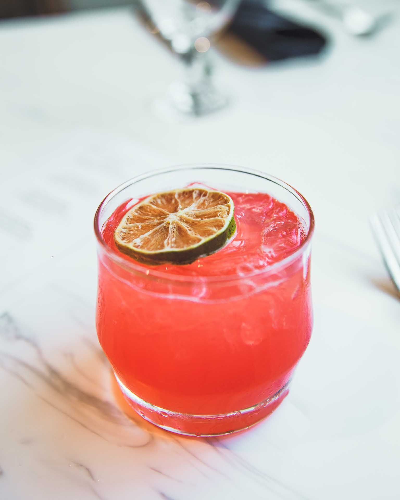 a glass of pink liquid with a lime slice on top