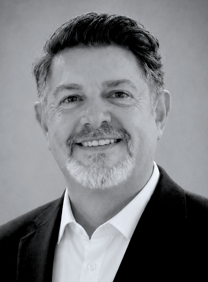 A man wearing glasses and a suit is smiling in a black and white photo.