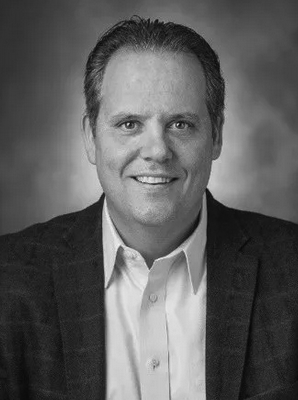 A man in a suit and white shirt is smiling in a black and white photo.
