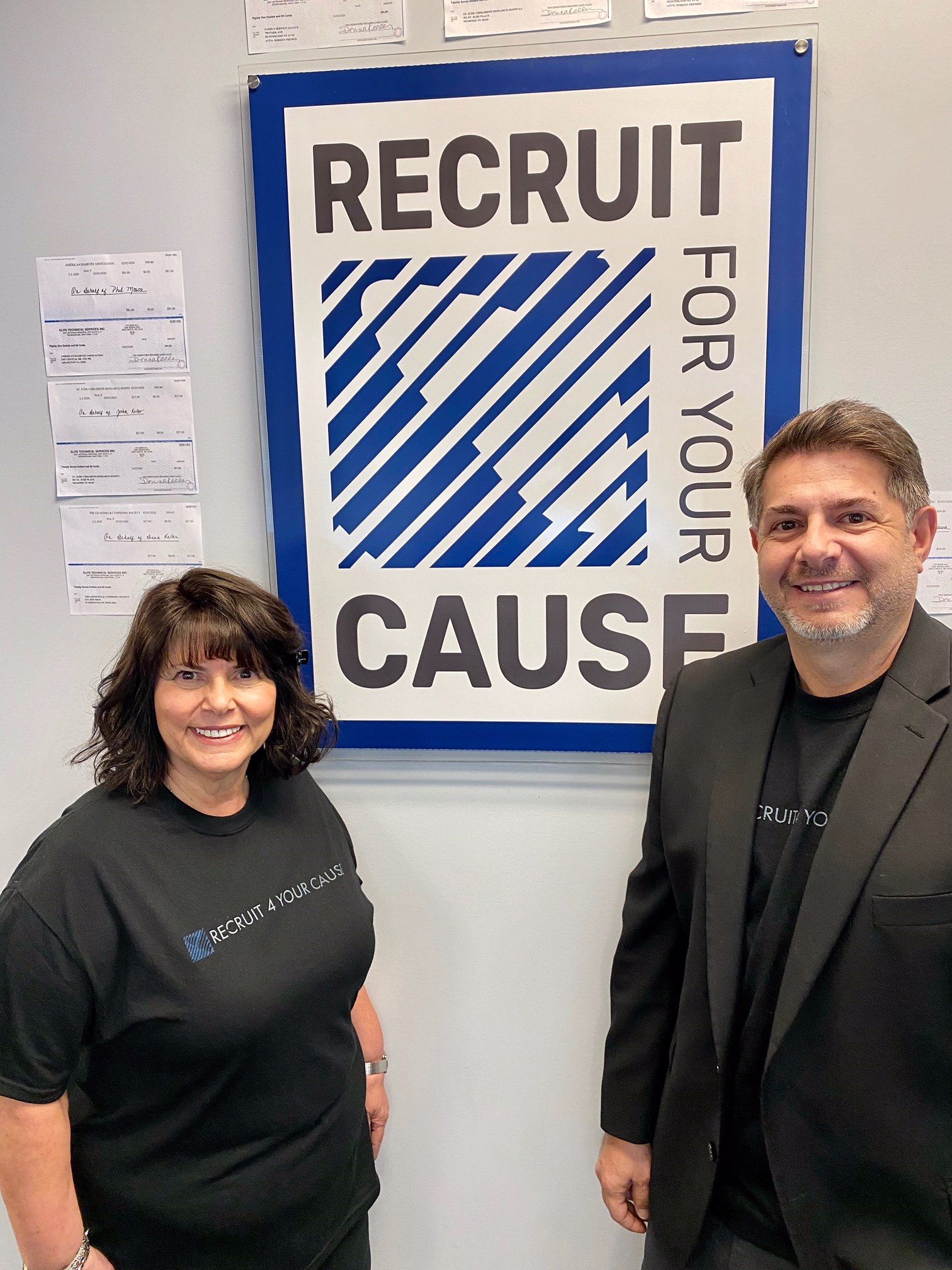 A man and a woman are standing in front of a recruit for your cause sign.