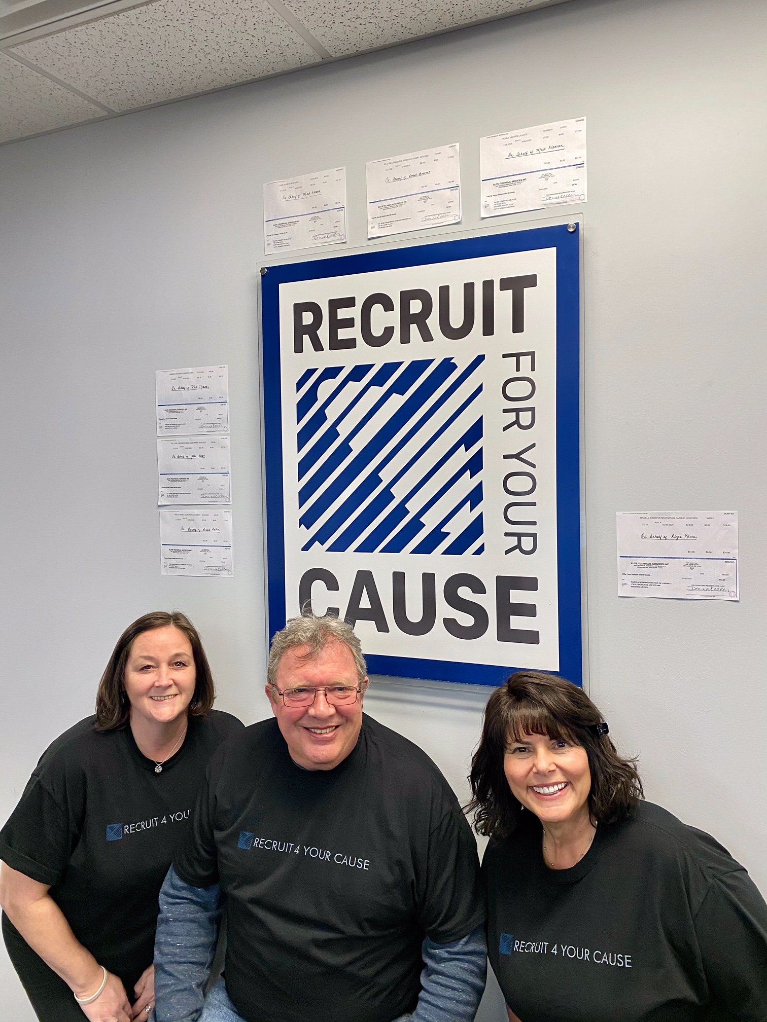 Three people are posing for a picture in front of a recruit for your cause sign.