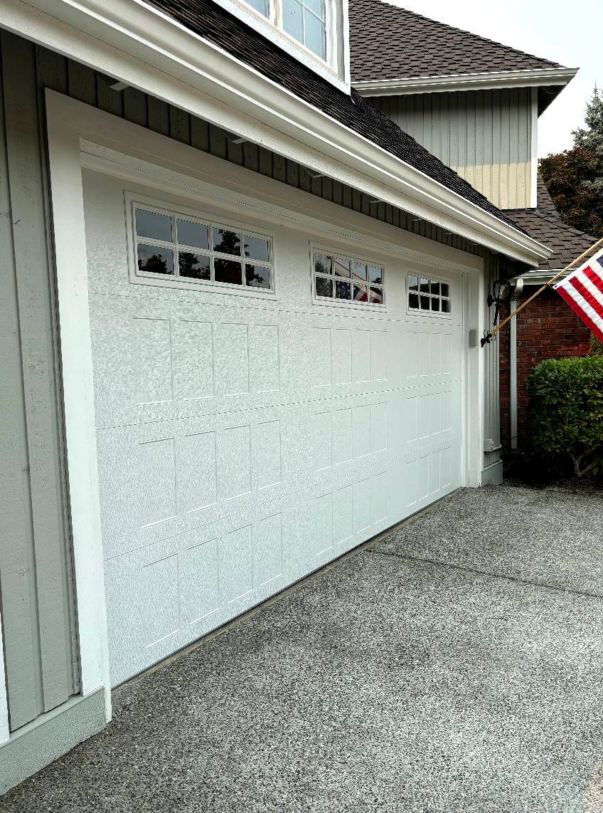 White garage door with small windows beside a gravel driveway and house exterior
