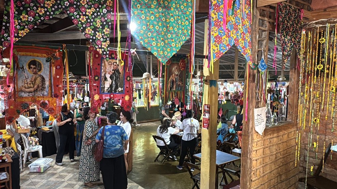 Interior festivo com pessoas, decorado com tecidos coloridos e arte religiosa.