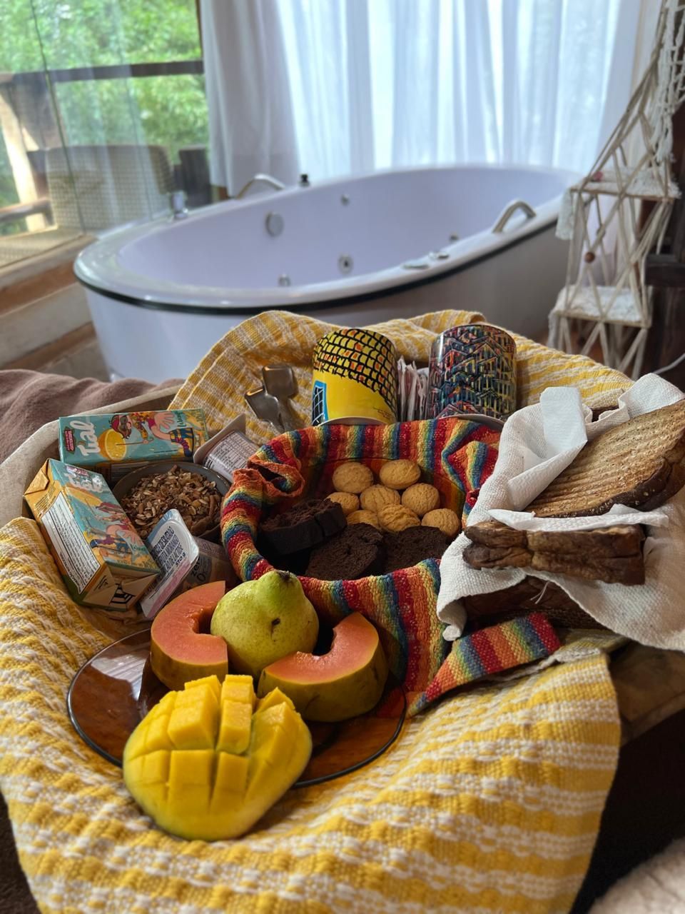 Cesta de alimentos, incluindo frutas e pães, disposta em frente a uma banheira de hidromassagem.