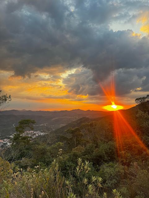 Pôr do sol sobre uma cordilheira com nuvens dramáticas e vibrantes tons de laranja e amarelo.