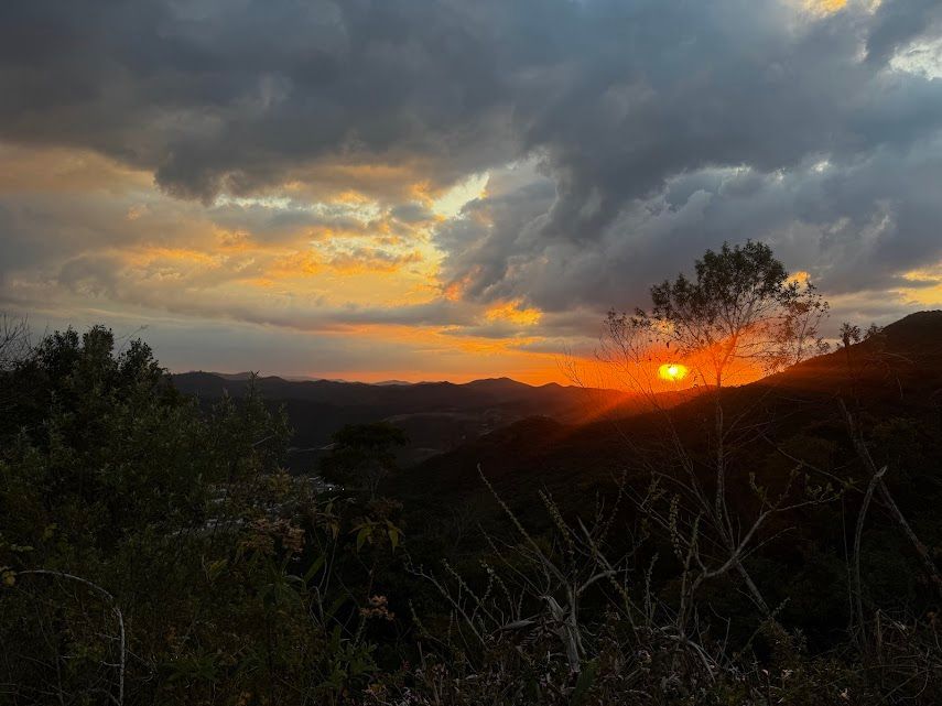 Pôr do sol sobre colinas recortadas com nuvens alaranjadas e escuras.