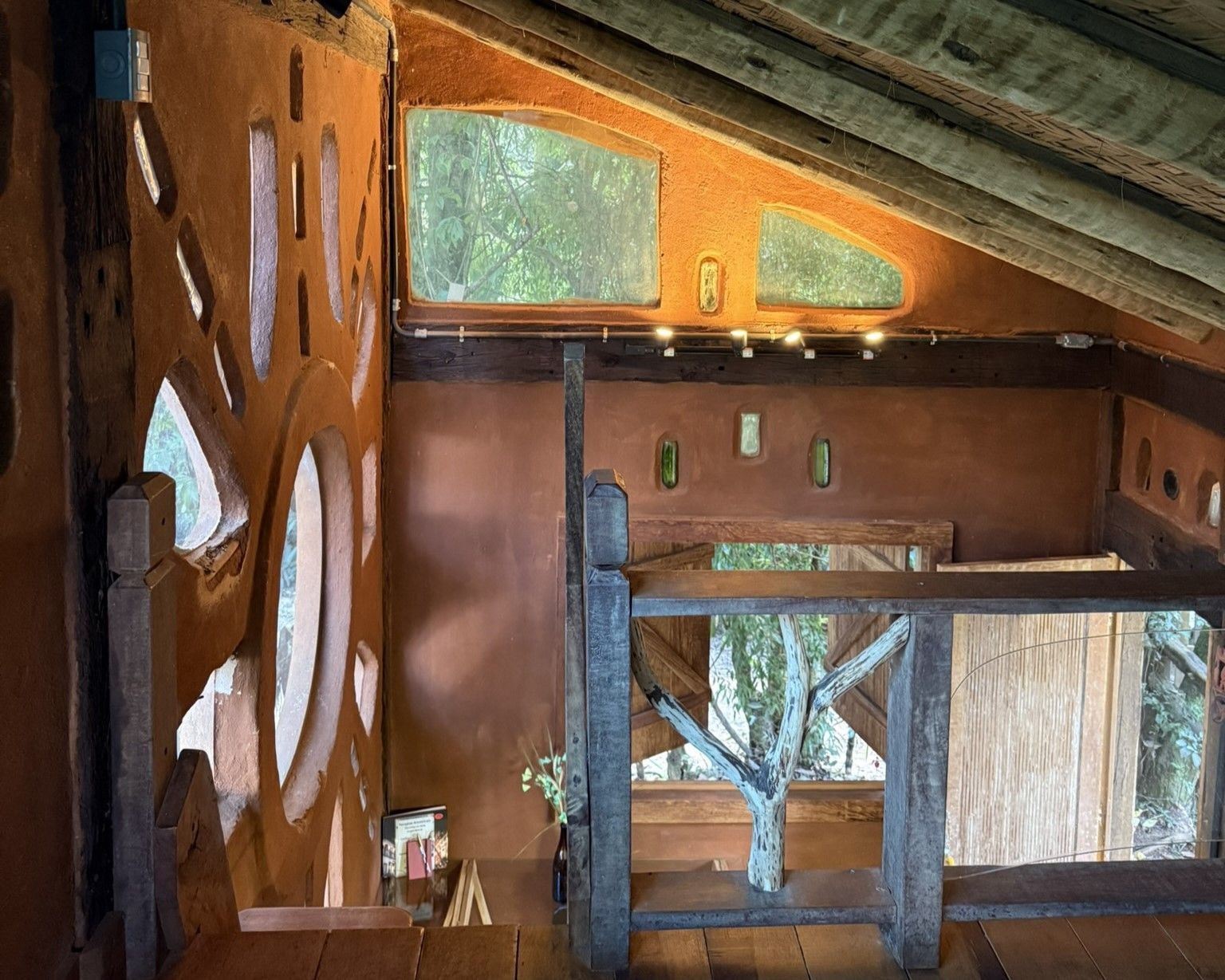 Interior de uma casa na árvore com paredes avermelhadas, recortes decorativos e um galho de árvore visível através de uma janela.
