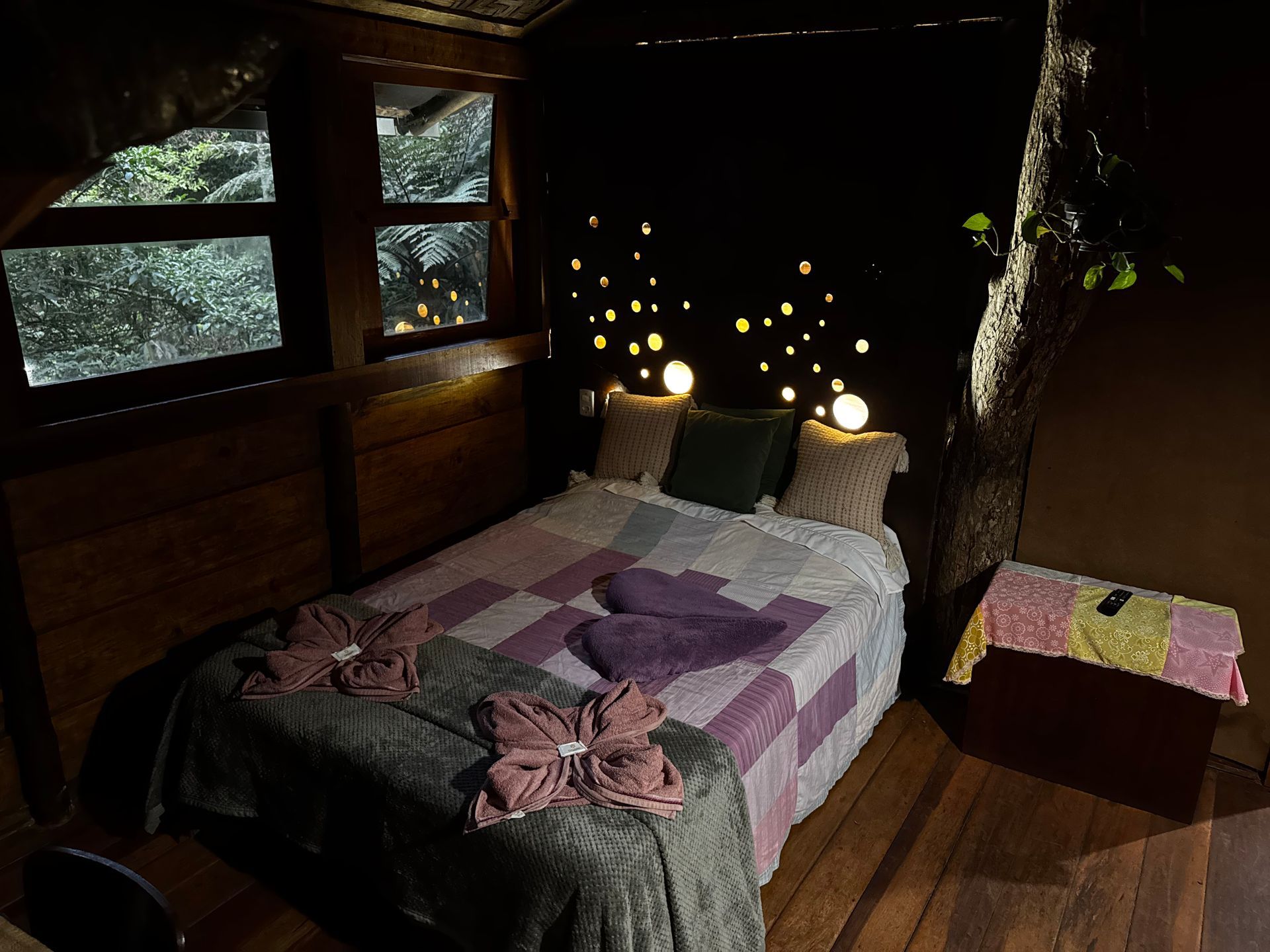 Quarto aconchegante em uma casa na árvore, com cama, luzes de fada e luz natural entrando pelas janelas.
