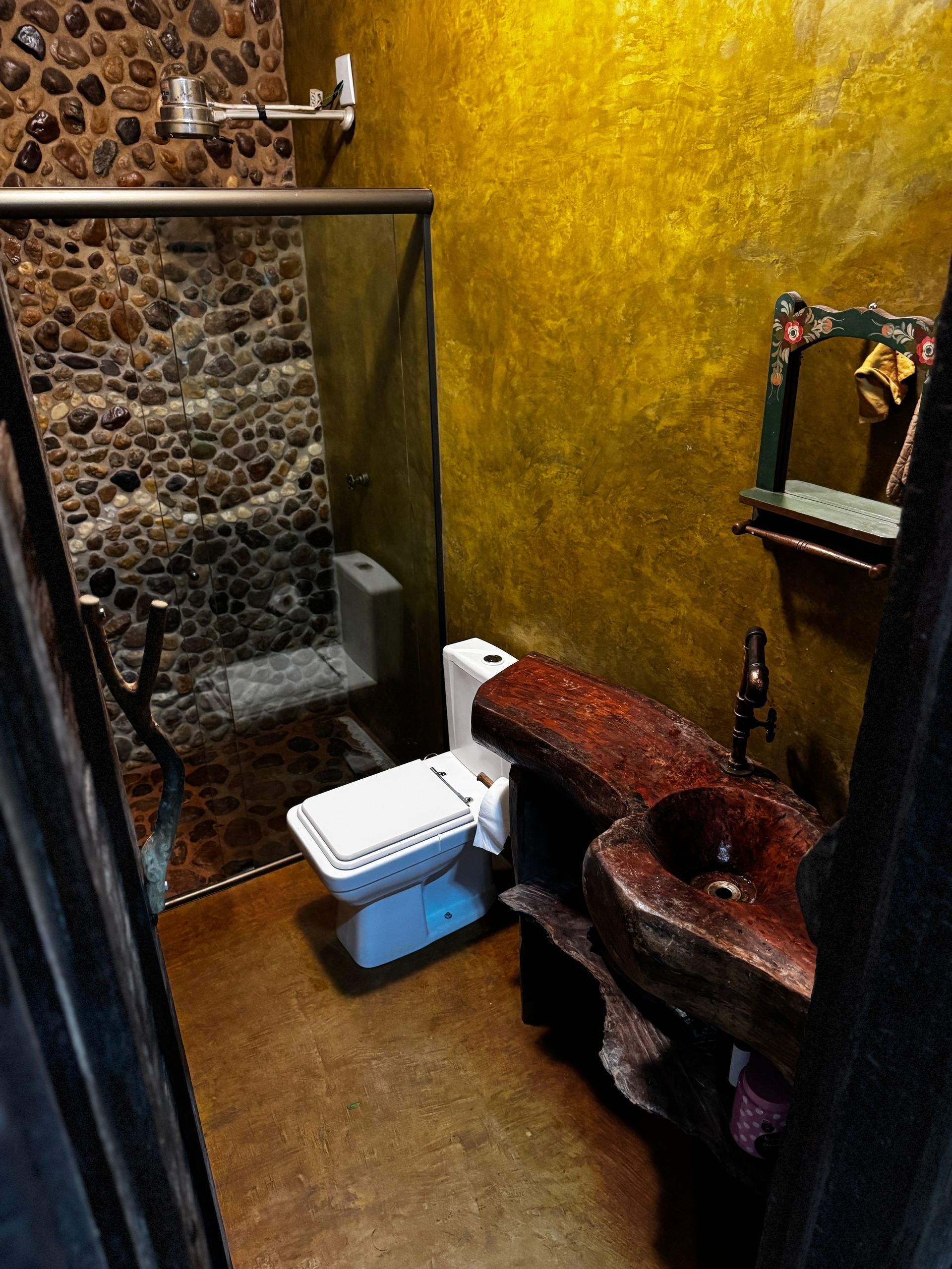 Banheiro com chuveiro de pedra, parede amarela, pia vermelha e vaso sanitário.