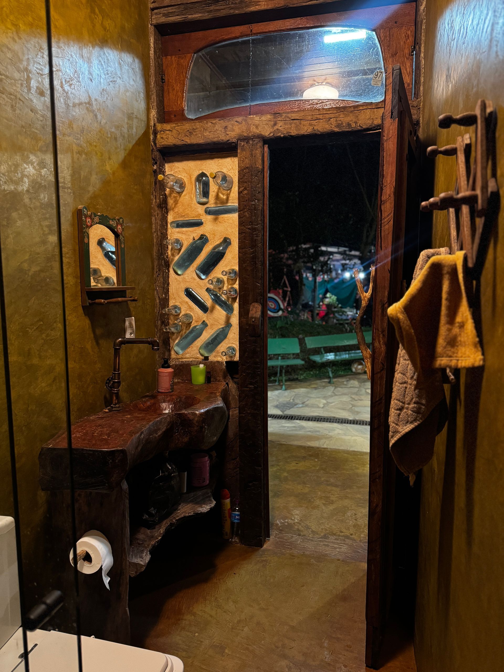 Interior de banheiro com moldura de porta de madeira rústica, pia e porta aberta para área de estar externa.