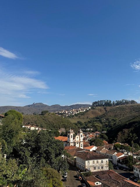 Vista panorâmica de uma cidade colonial aninhada em um vale, com igrejas brancas, telhados de telha vermelha e um céu azul brilhante.