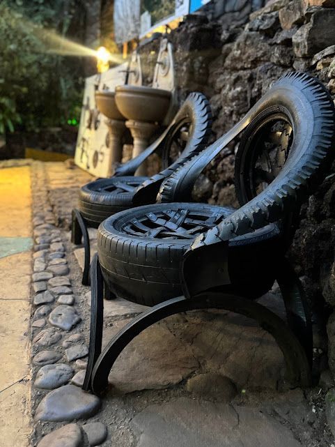 Duas cadeiras feitas de pneus estão dispostas em uma passarela de pedra ao lado de um muro de pedra.