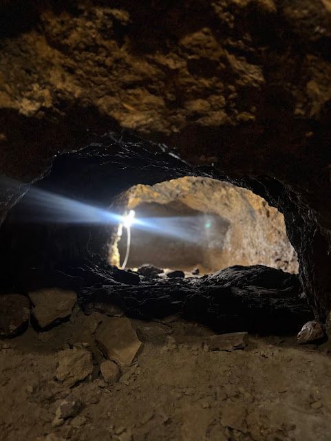 Abertura de caverna com luz intensa entrando pelo vão. Interior da caverna, paredes em tons terrosos.