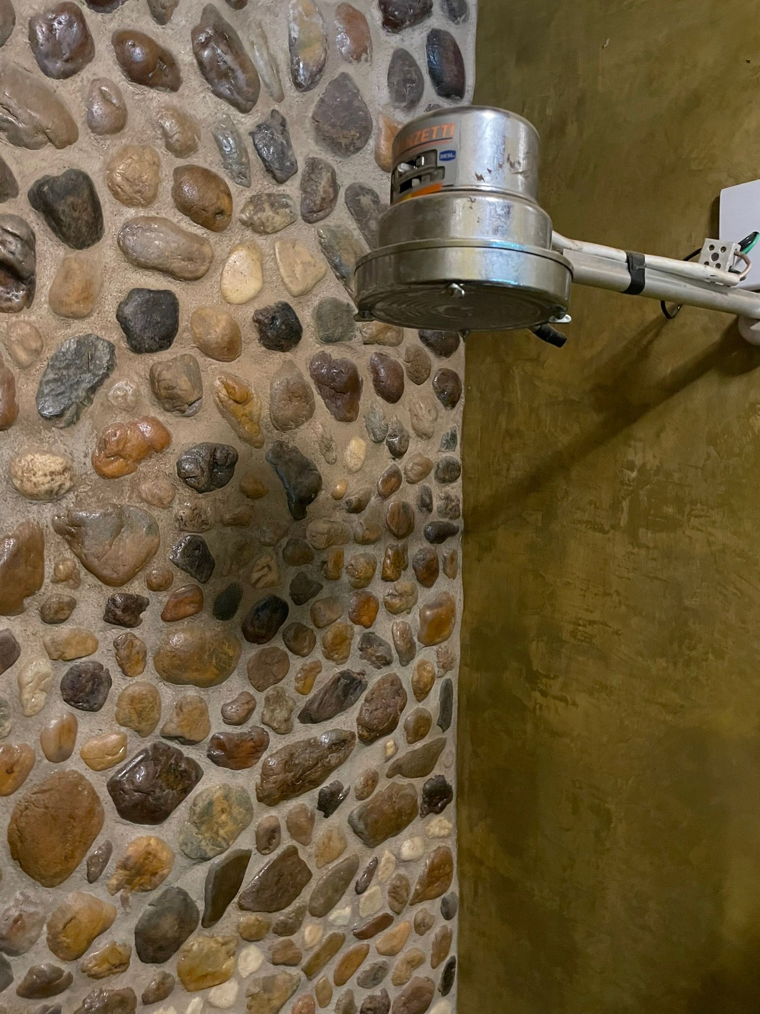 Uma lixadeira de chão prateada sobre uma parede de pedras de rio multicoloridas e uma parede dourada.