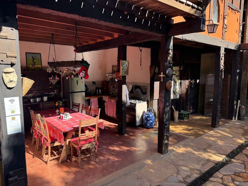 Cozinha e área de jantar externas com mesa e cadeiras vermelhas sob uma pérgola de madeira.