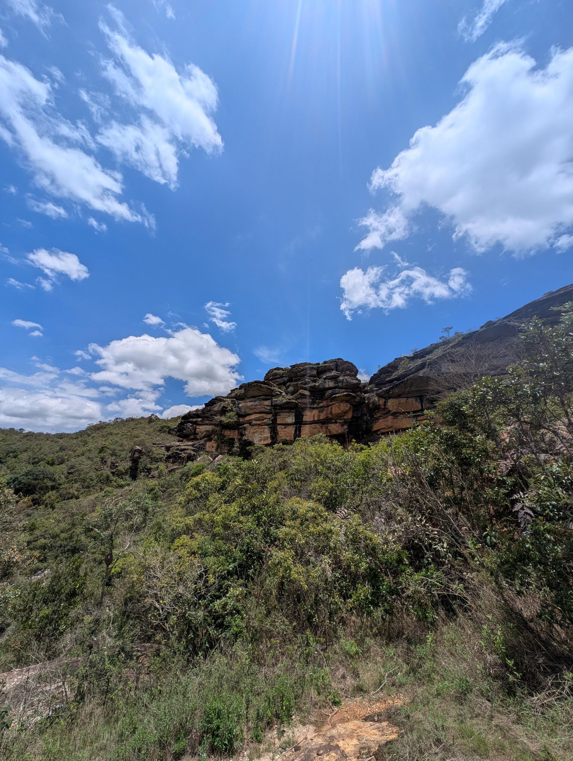 Encosta com formação rochosa sob céu azul com nuvens fofas.