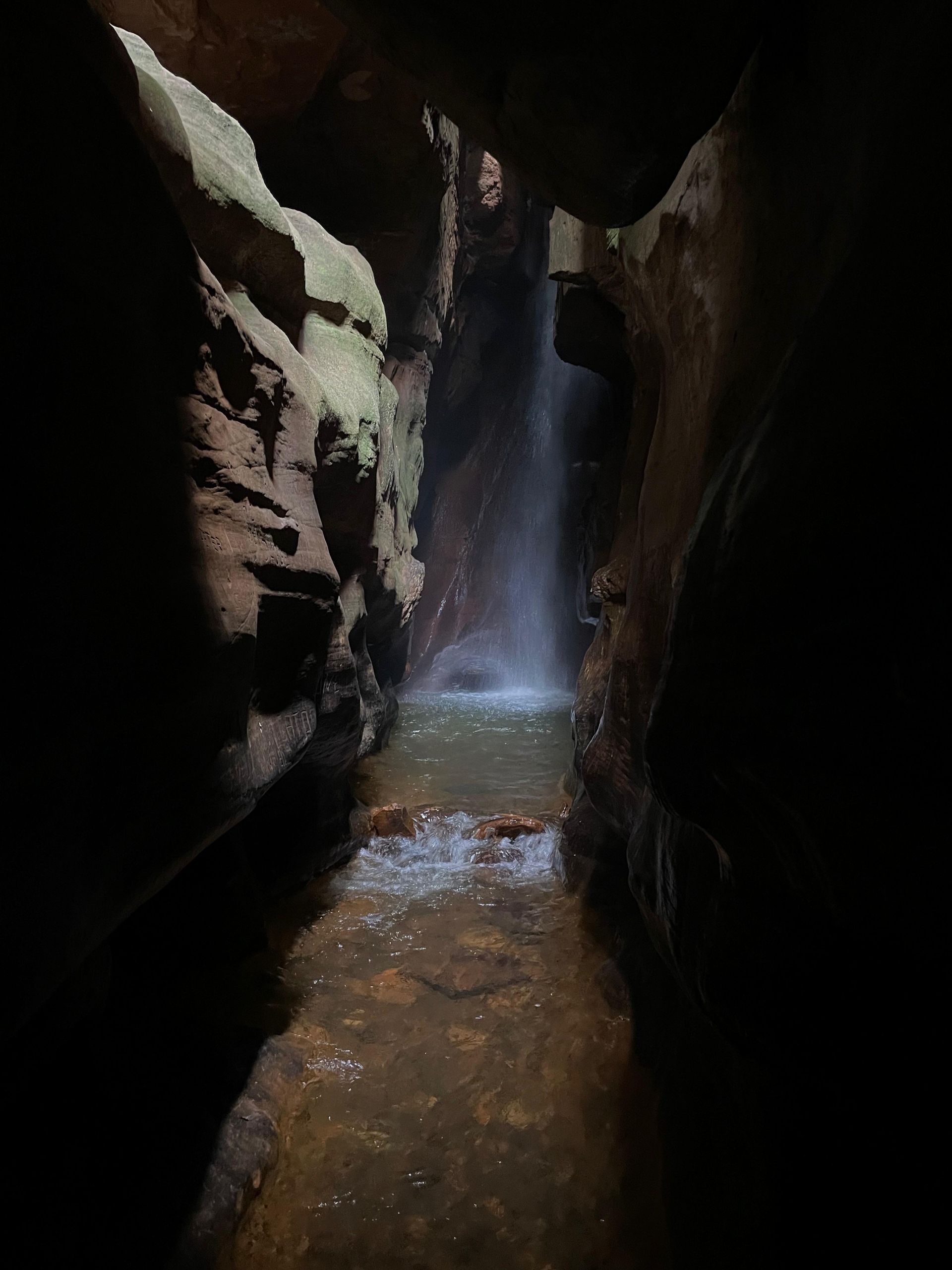 Cachoeira que deságua em uma pequena piscina dentro de uma caverna escura e rochosa.