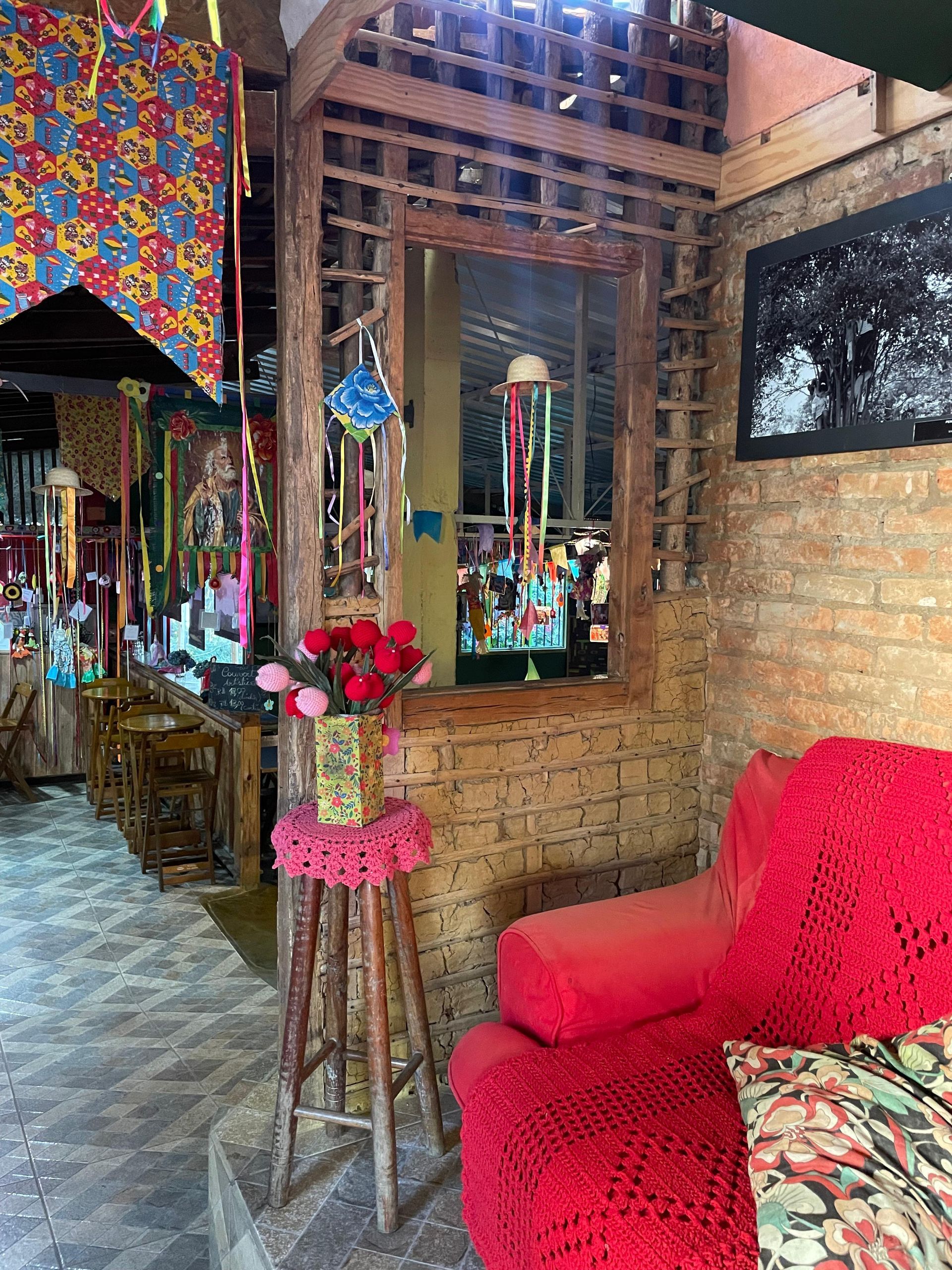 Interior aconchegante com sofá vermelho, parede de tijolos, detalhes em madeira e decoração colorida.