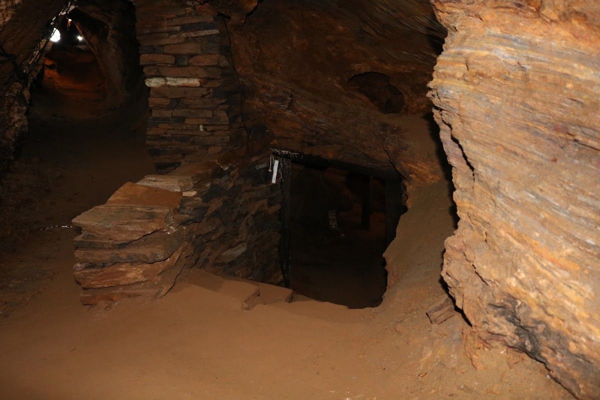 Túnel escavado na rocha, com degraus de pedra e uma abertura escura. Predominam as cores marrom e bege.