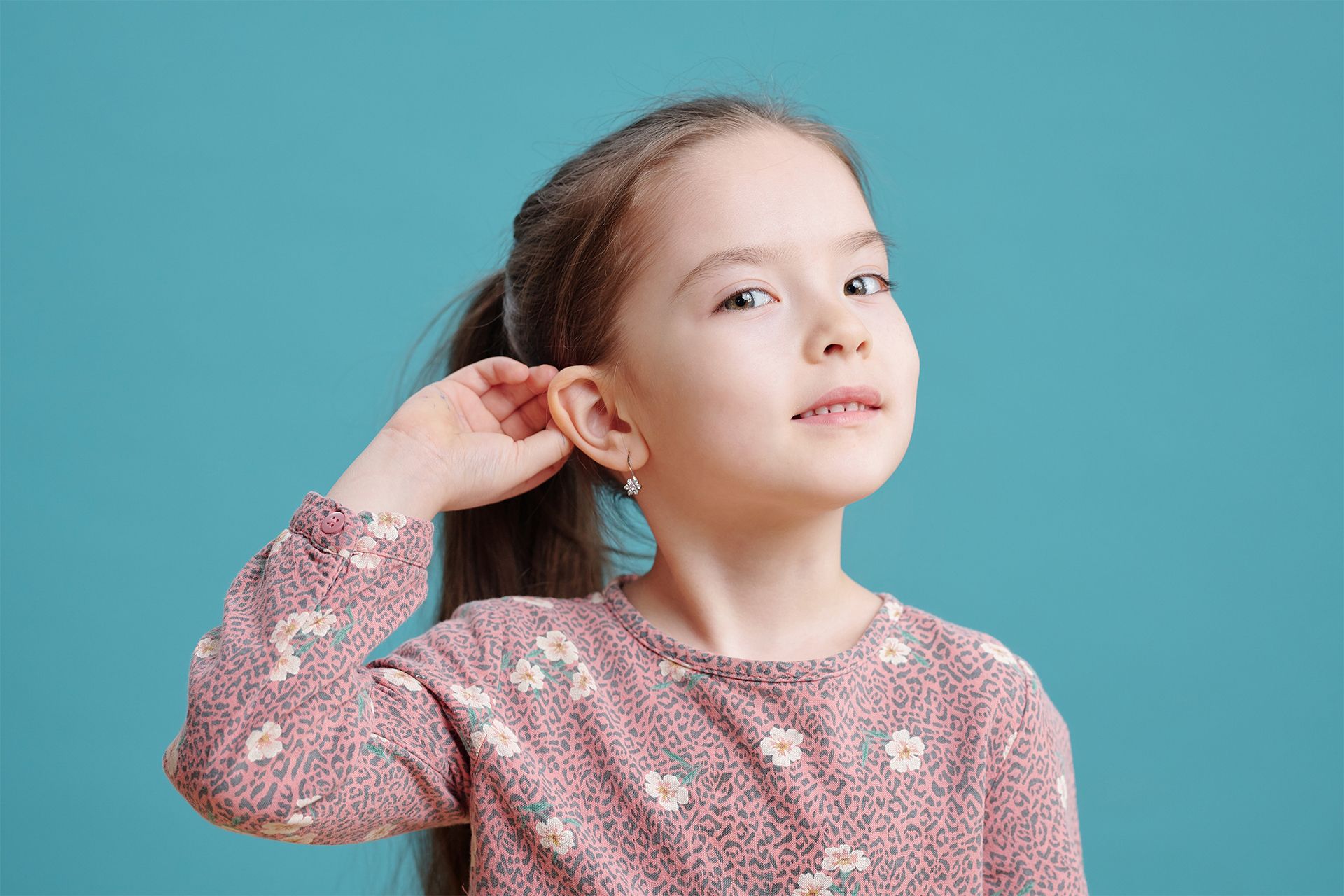 Girl with ponytail, touching ear, looking upwards with a slight smile, against a teal background. Girl with ponytail, touching ear, looking upwards with a slight smile, against a teal background.