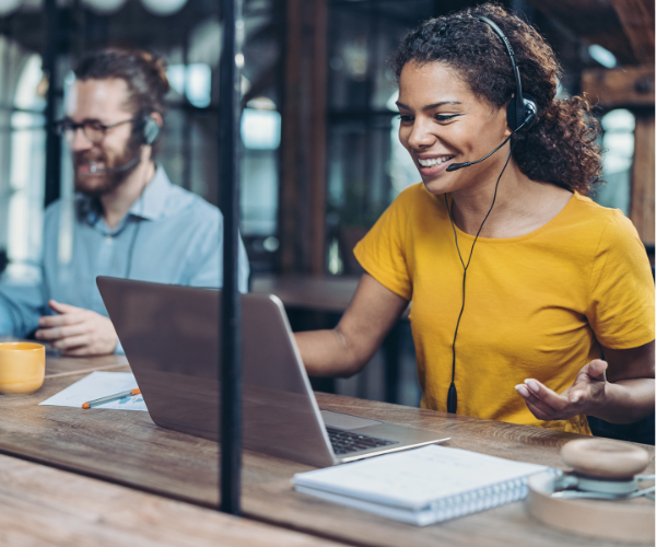 Una mujer con auriculares está sentada en un escritorio usando una computadora portátil.