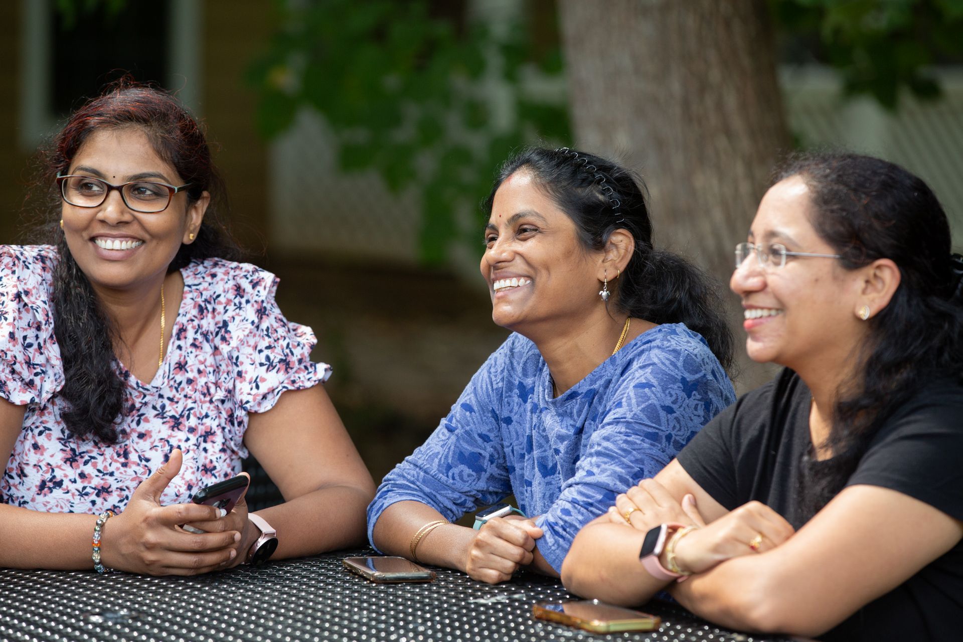 Three women are sitting at a table with their arms crossed and smiling.