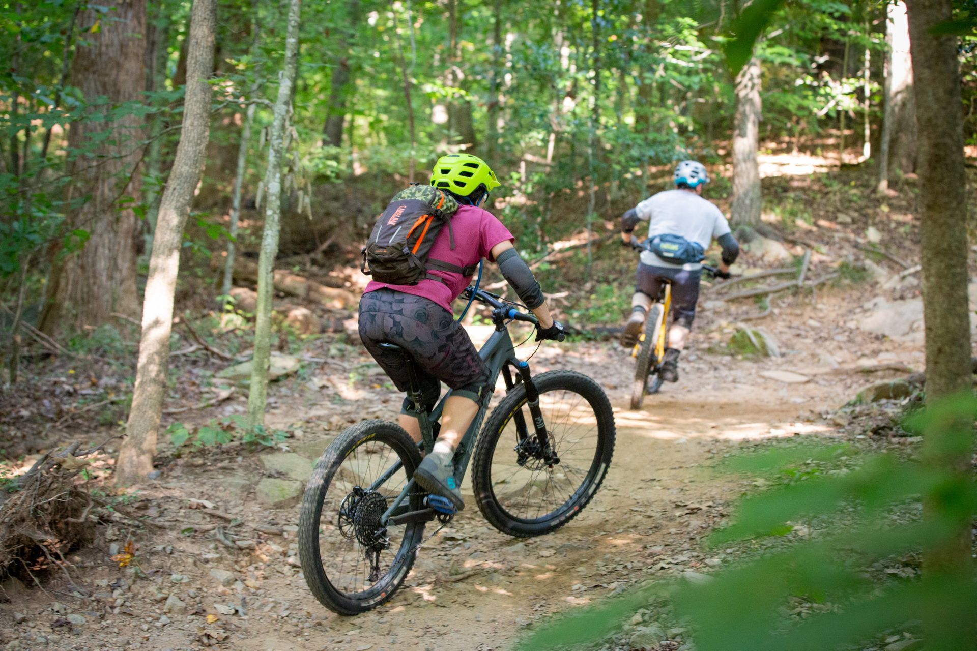 Two people are riding bikes on a trail in the woods.