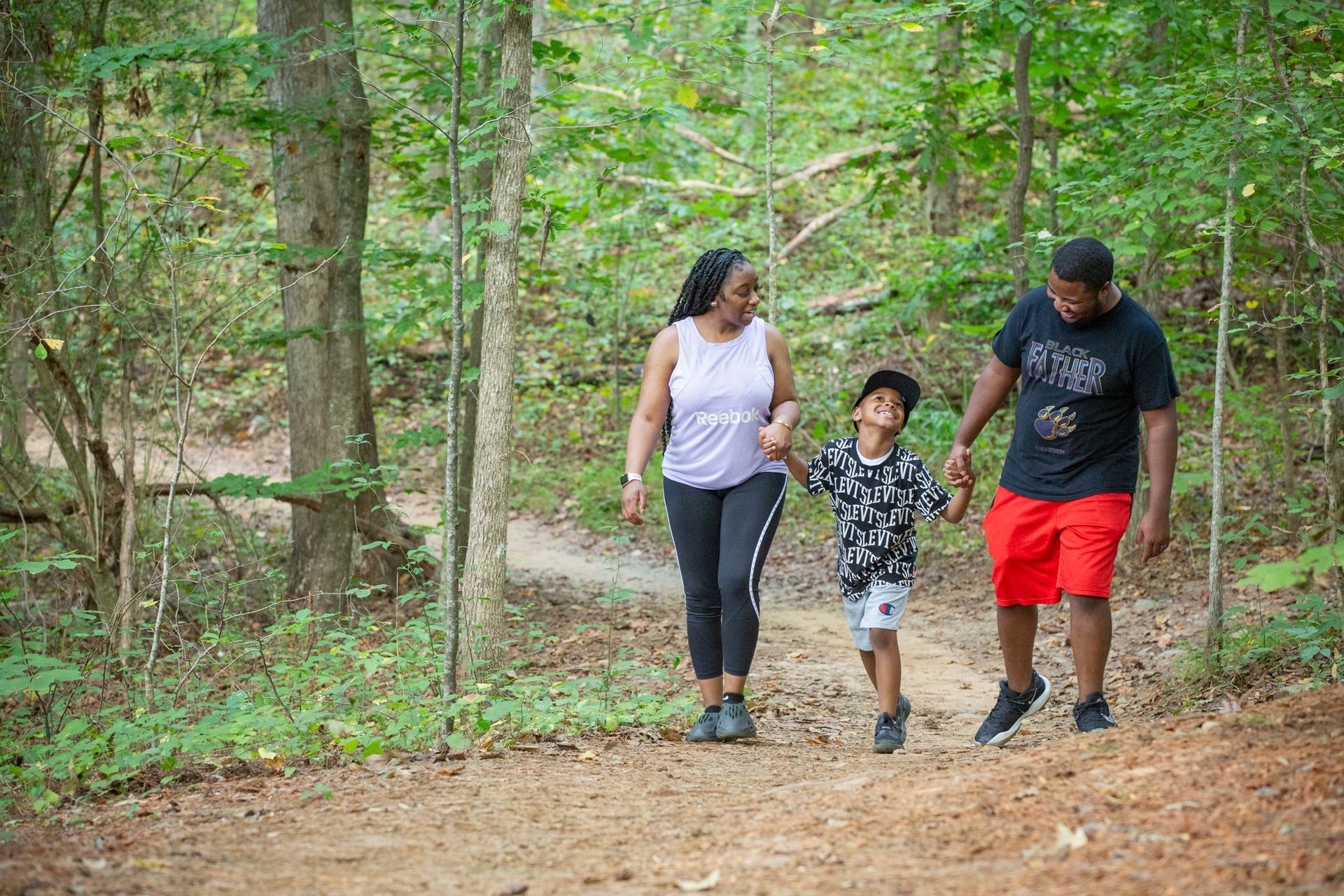 A family is walking down a path in the woods holding hands.