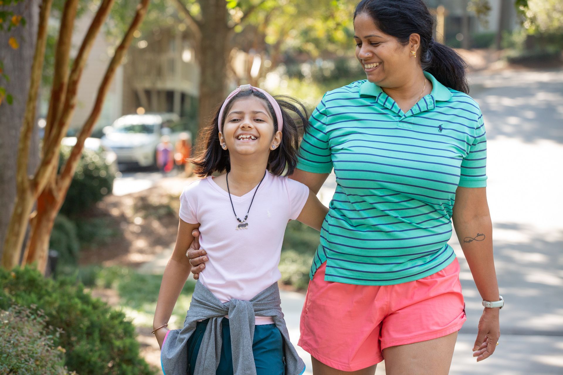 A woman and a little girl are walking down a sidewalk.