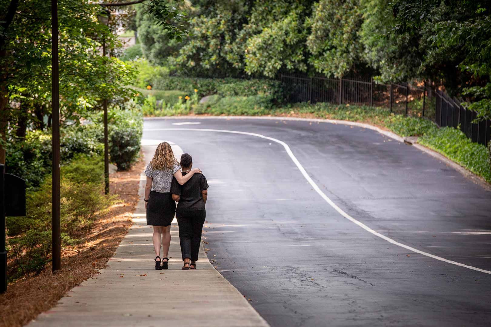 Two women are walking down a sidewalk next to a road.