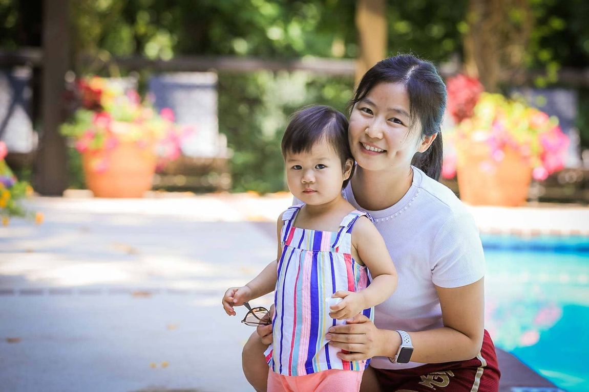 A woman is holding a little girl in her arms in front of a pool.