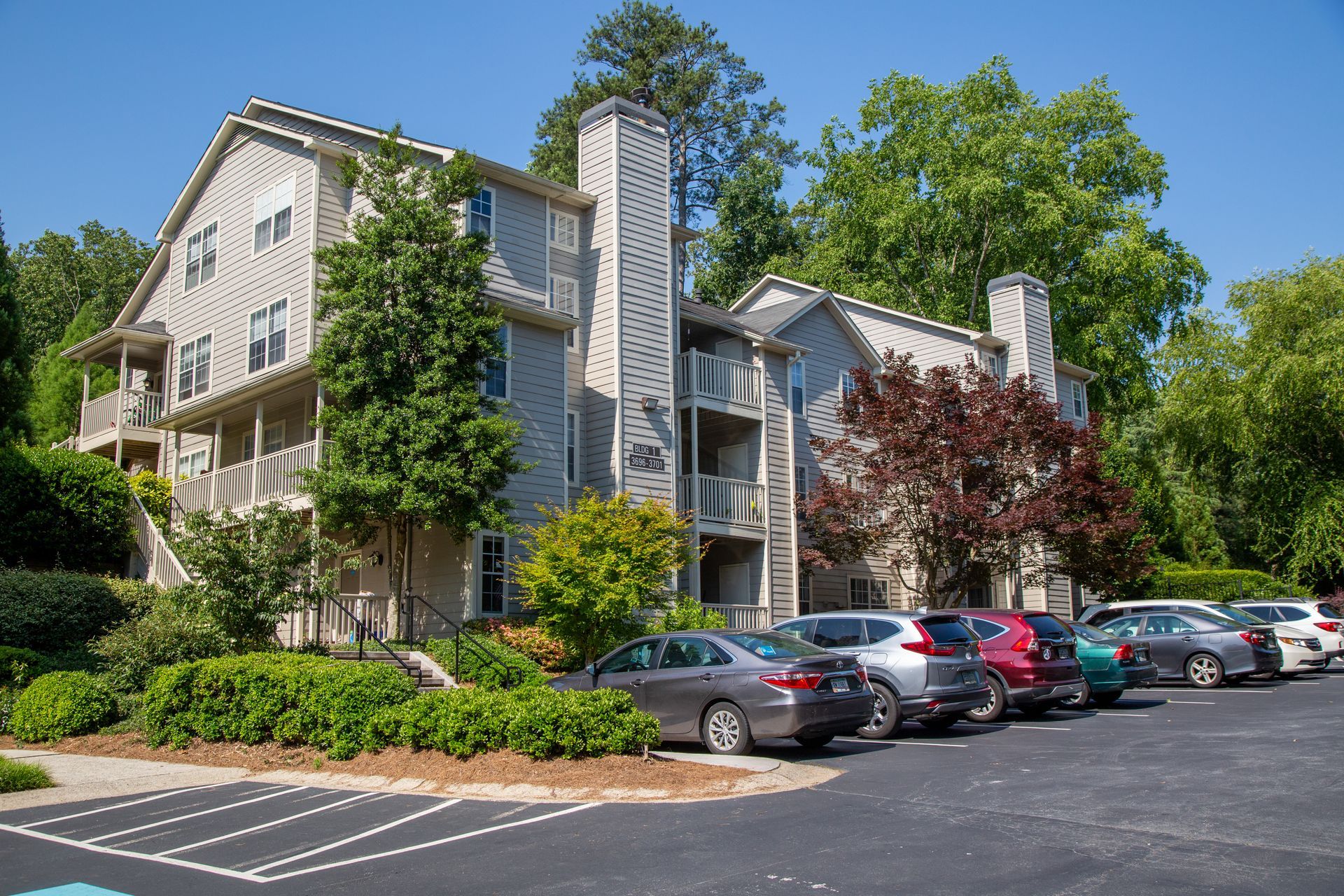 A row of cars are parked in front of a large apartment building.