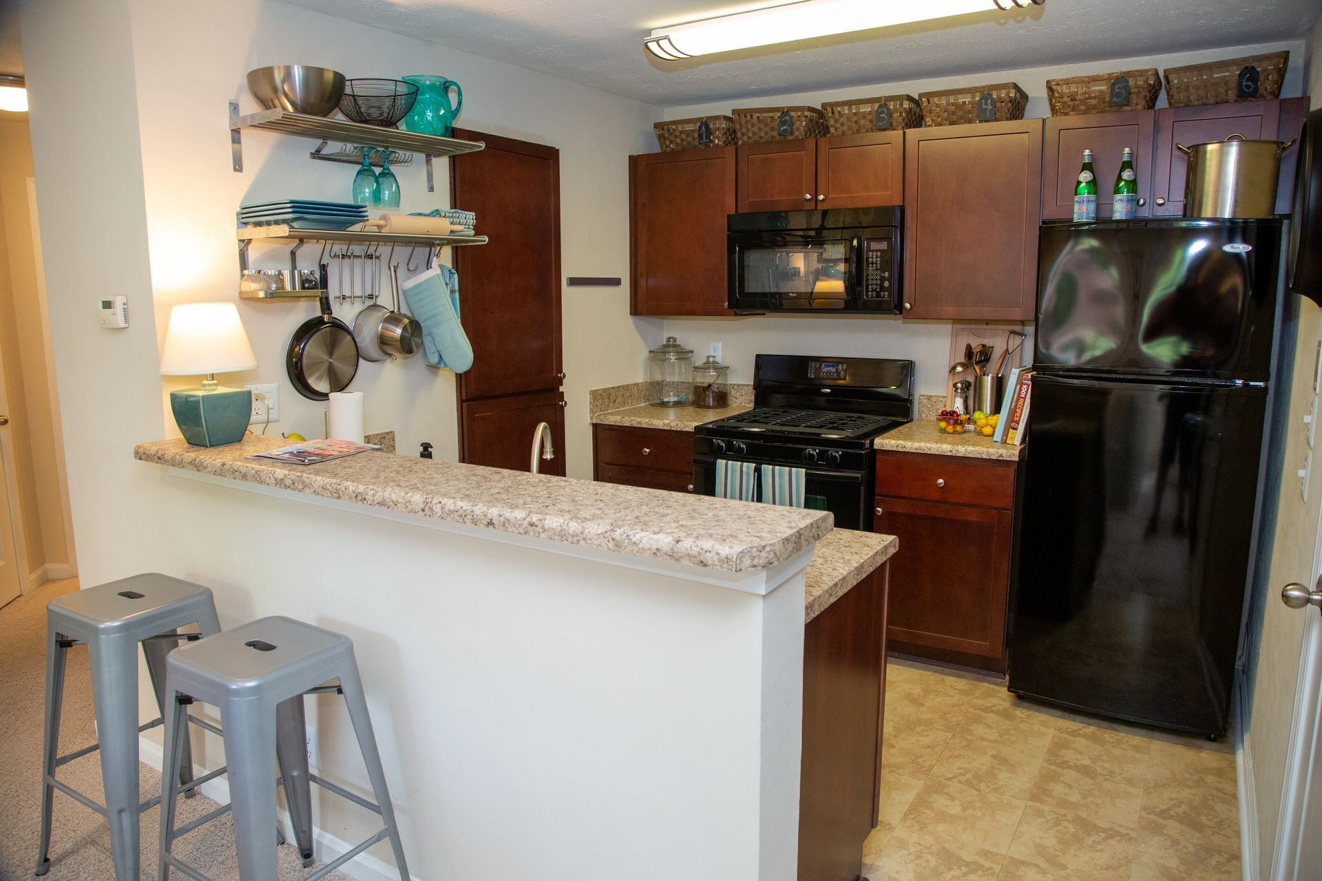 A kitchen with a stove , refrigerator , microwave and stools