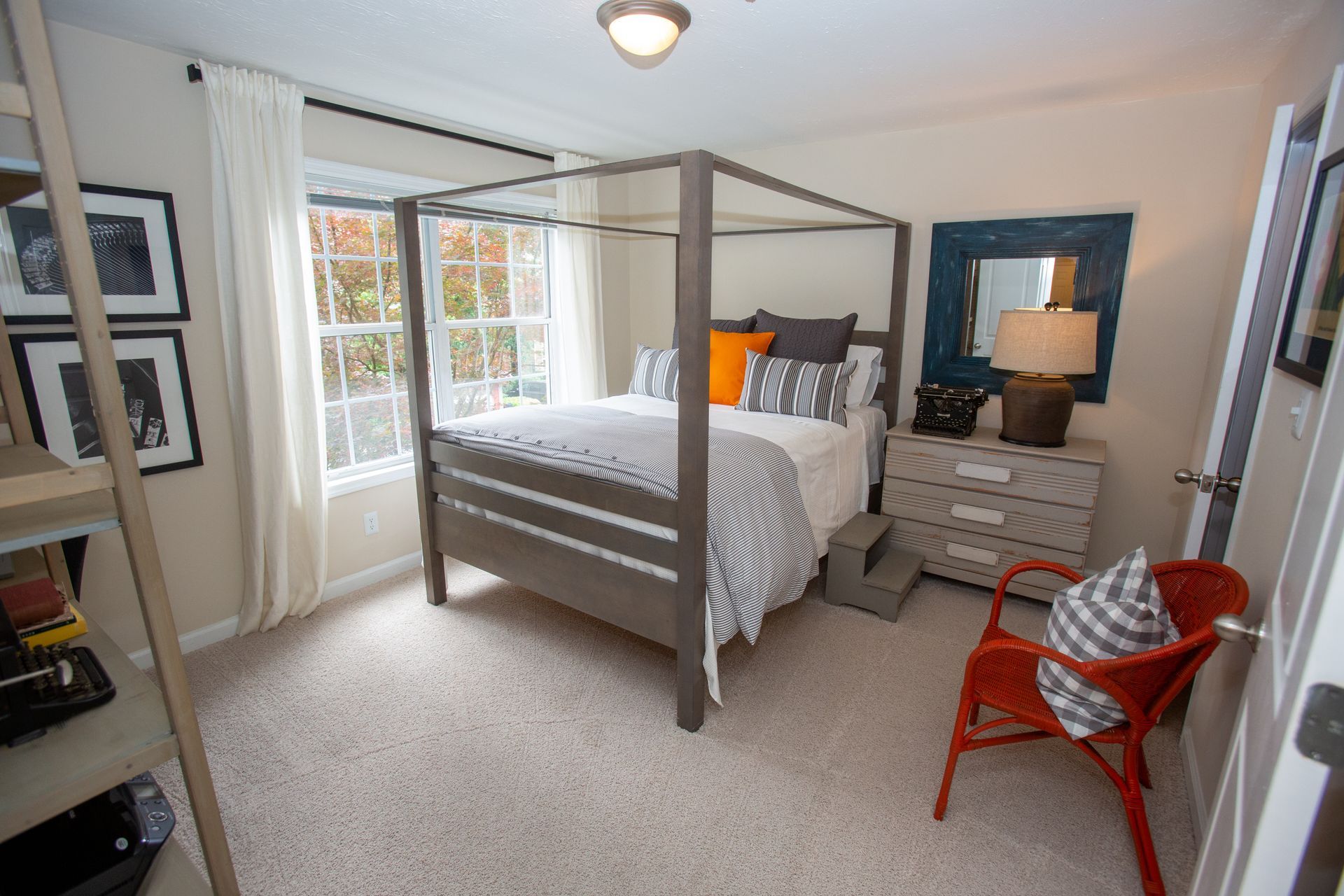A bedroom with a four poster bed , dresser , chair and window.