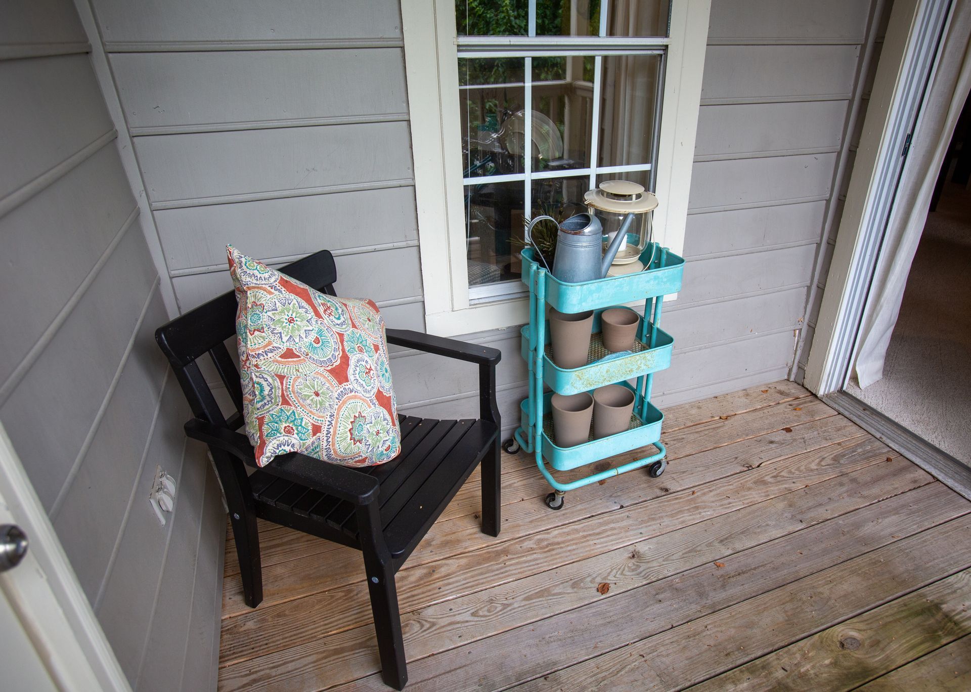 There is a chair and a cart with pots on it on the porch.