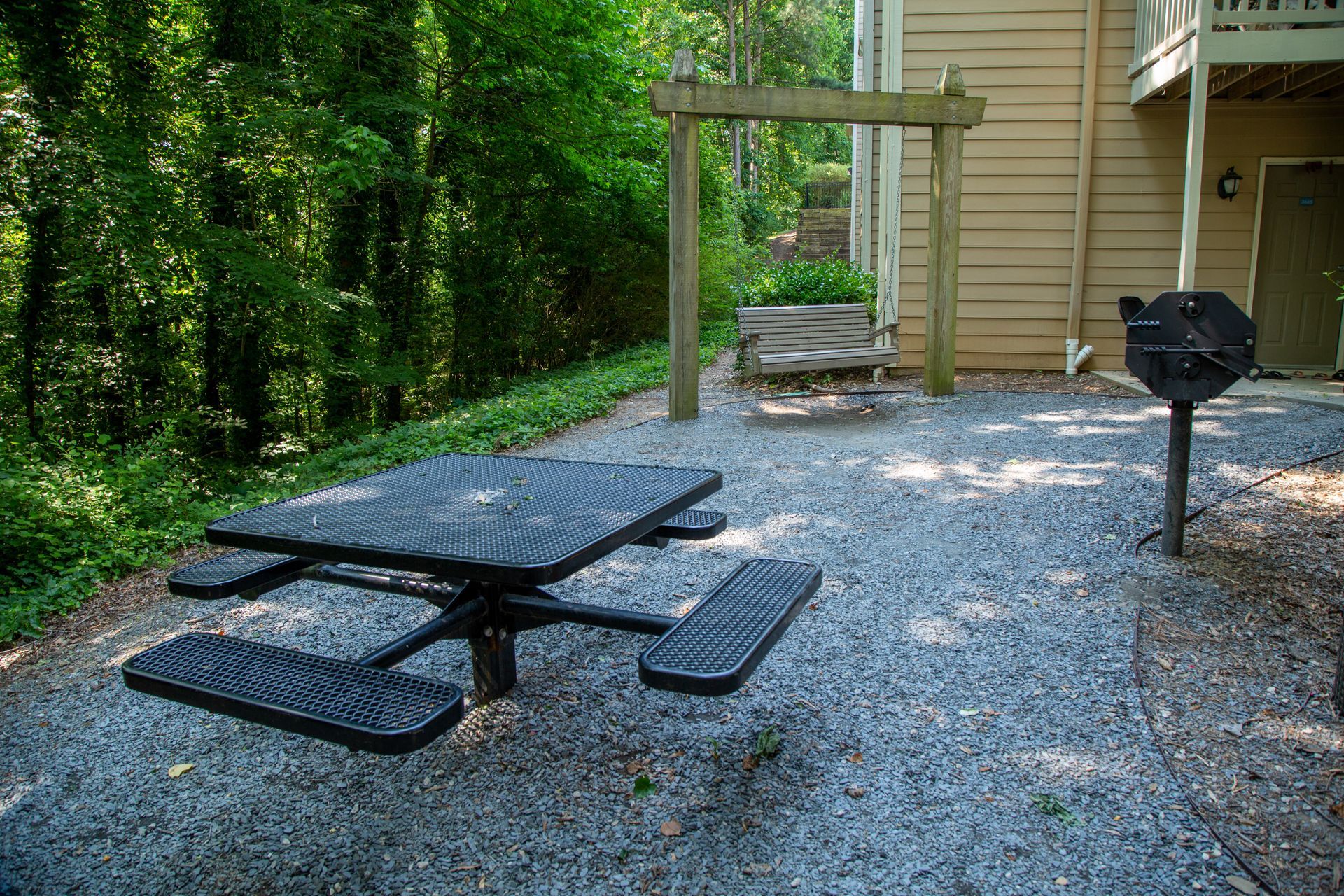 A picnic table and grill are in a gravel area in front of a house.