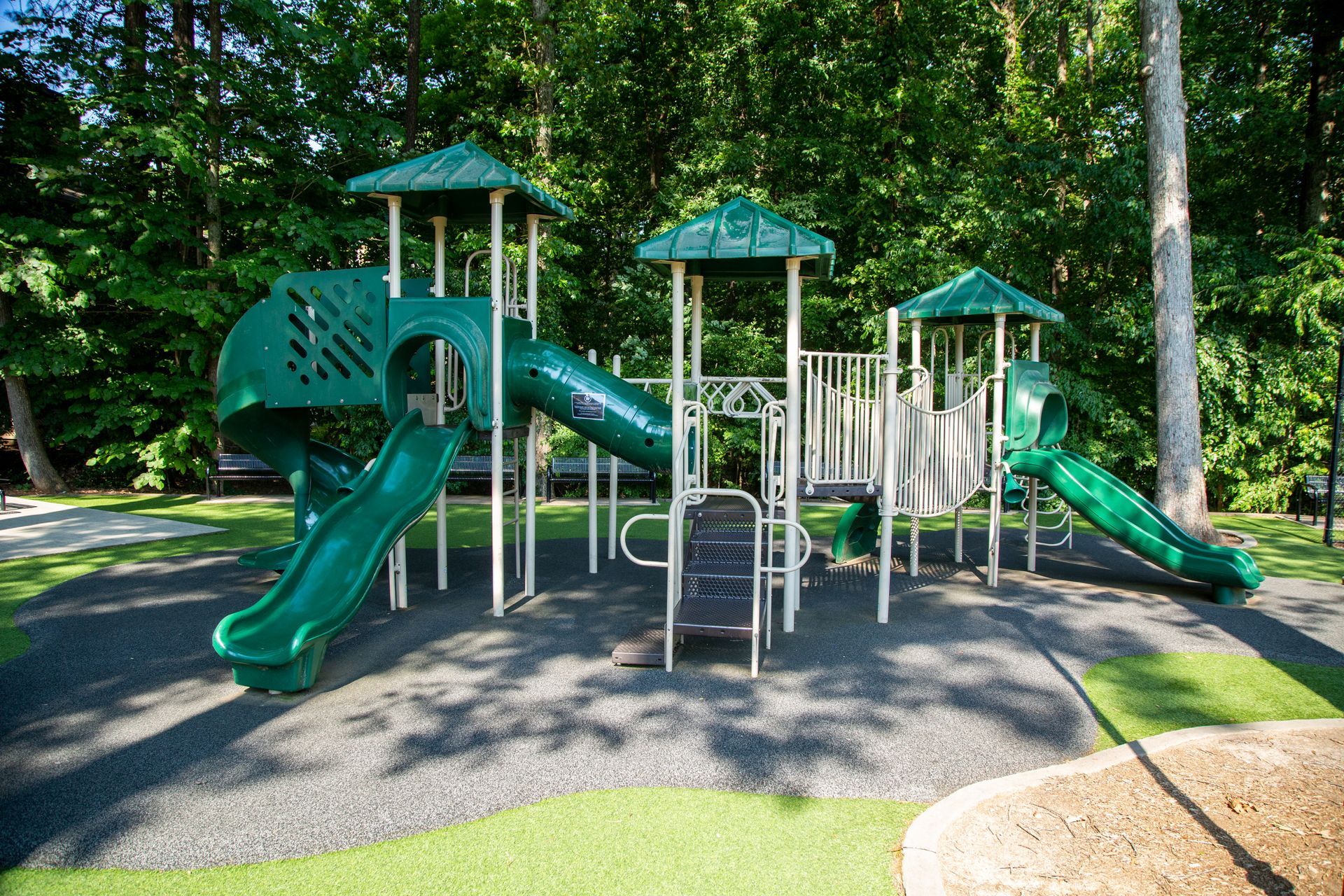 A green playground set in a park with trees in the background.