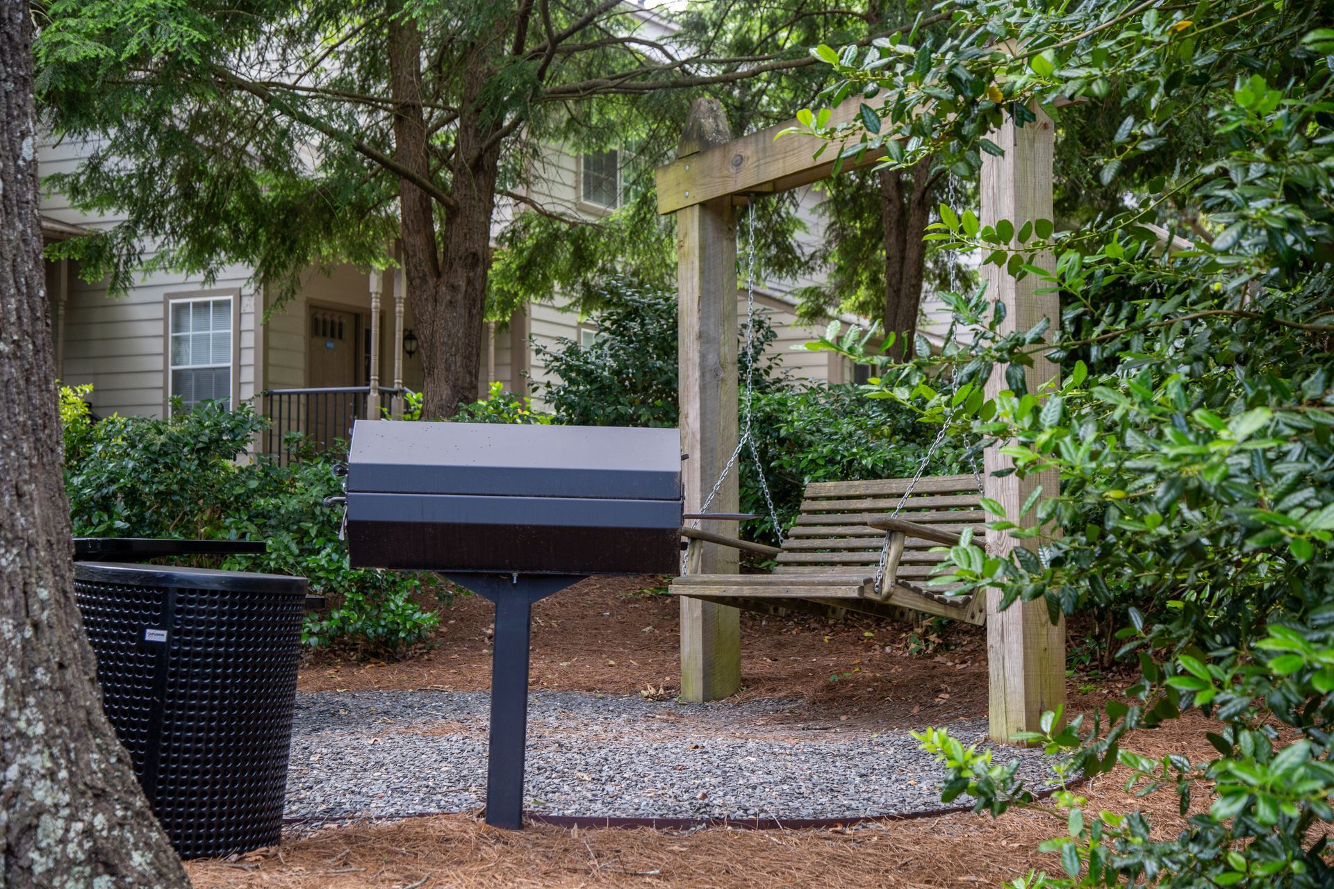 A barbecue grill is sitting next to a wooden swing in a park.