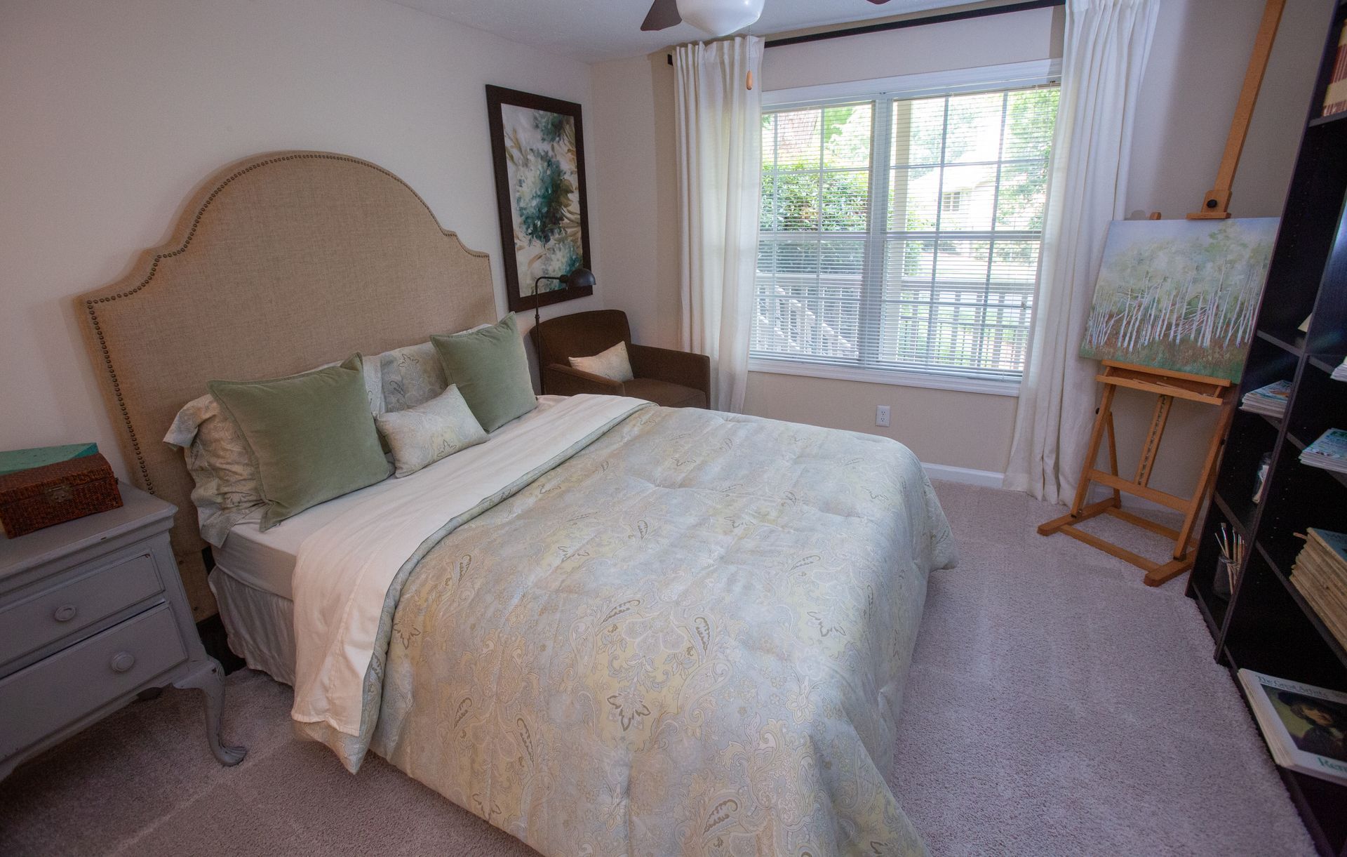 A bedroom with a bed , nightstand , painting easel and window.