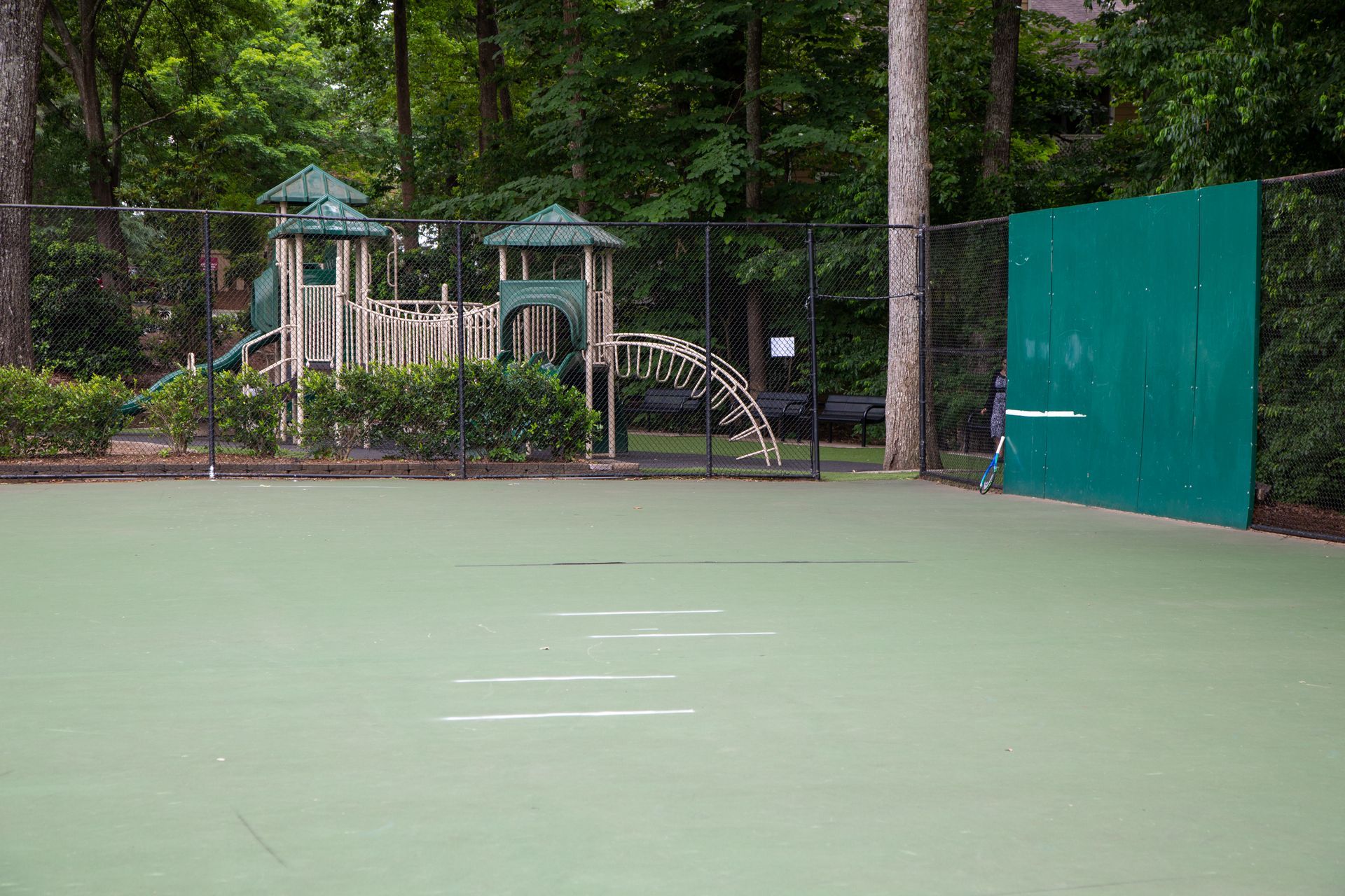 An empty tennis court with a playground in the background.
