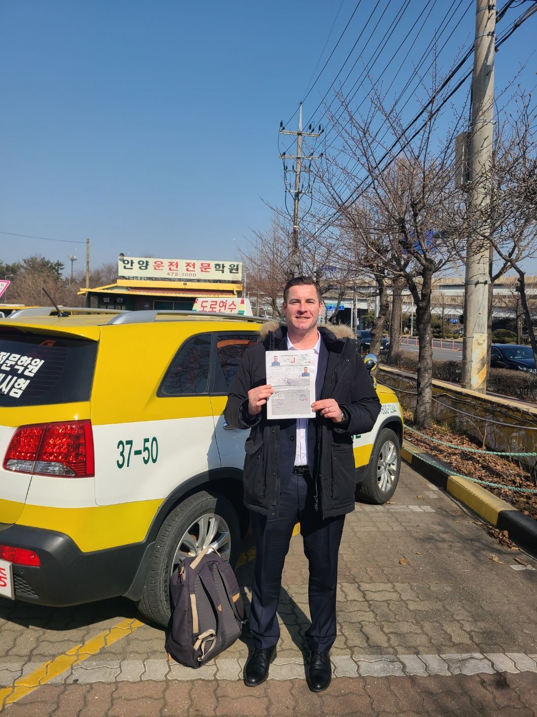Man holding a document next to a yellow SUV, likely after passing a driving test.