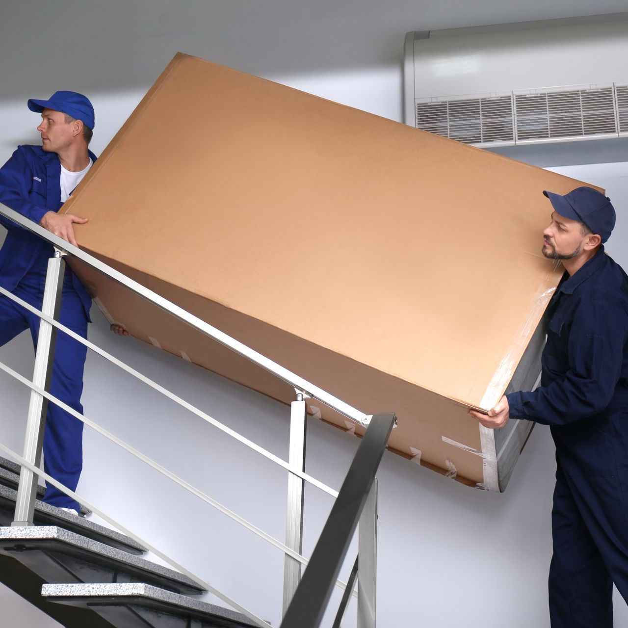 two men are carrying a large cardboard box up a set of stairs .