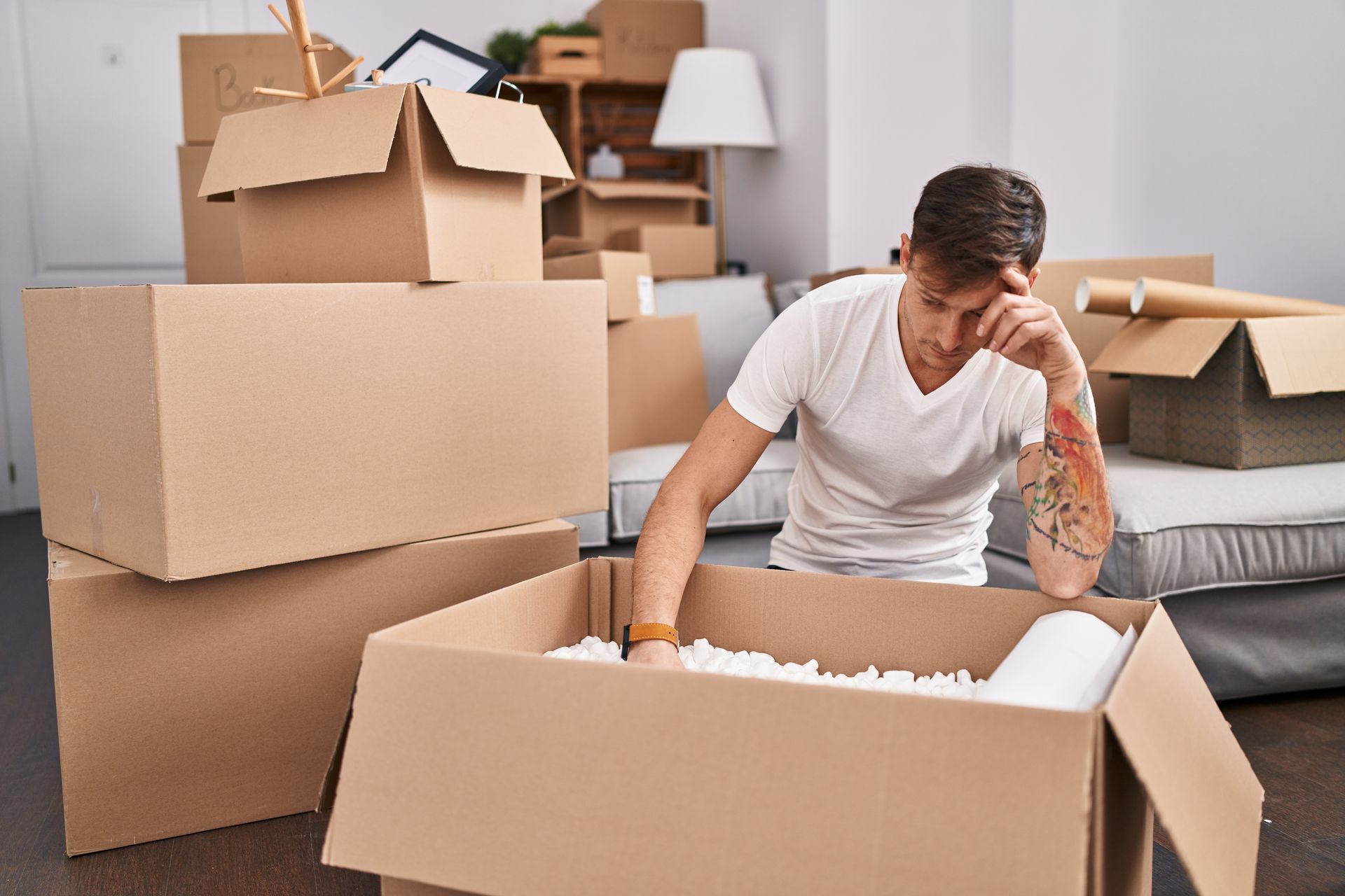 a man is sitting in a living room surrounded by cardboard boxes .