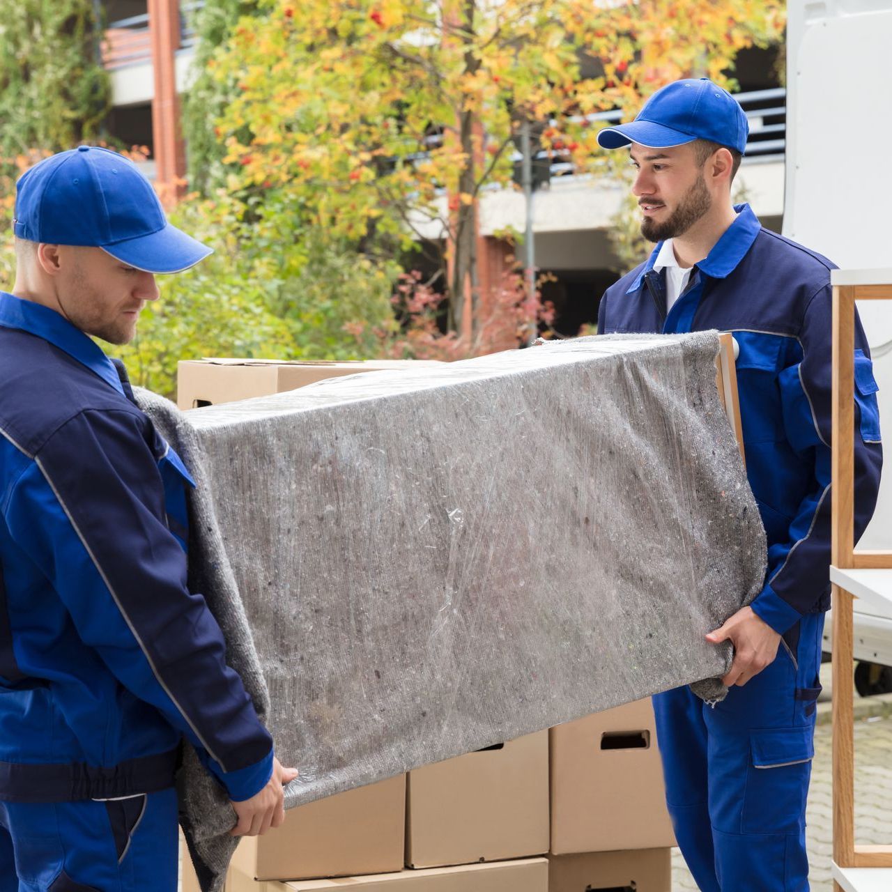two men in blue uniforms are carrying a large piece of furniture .
