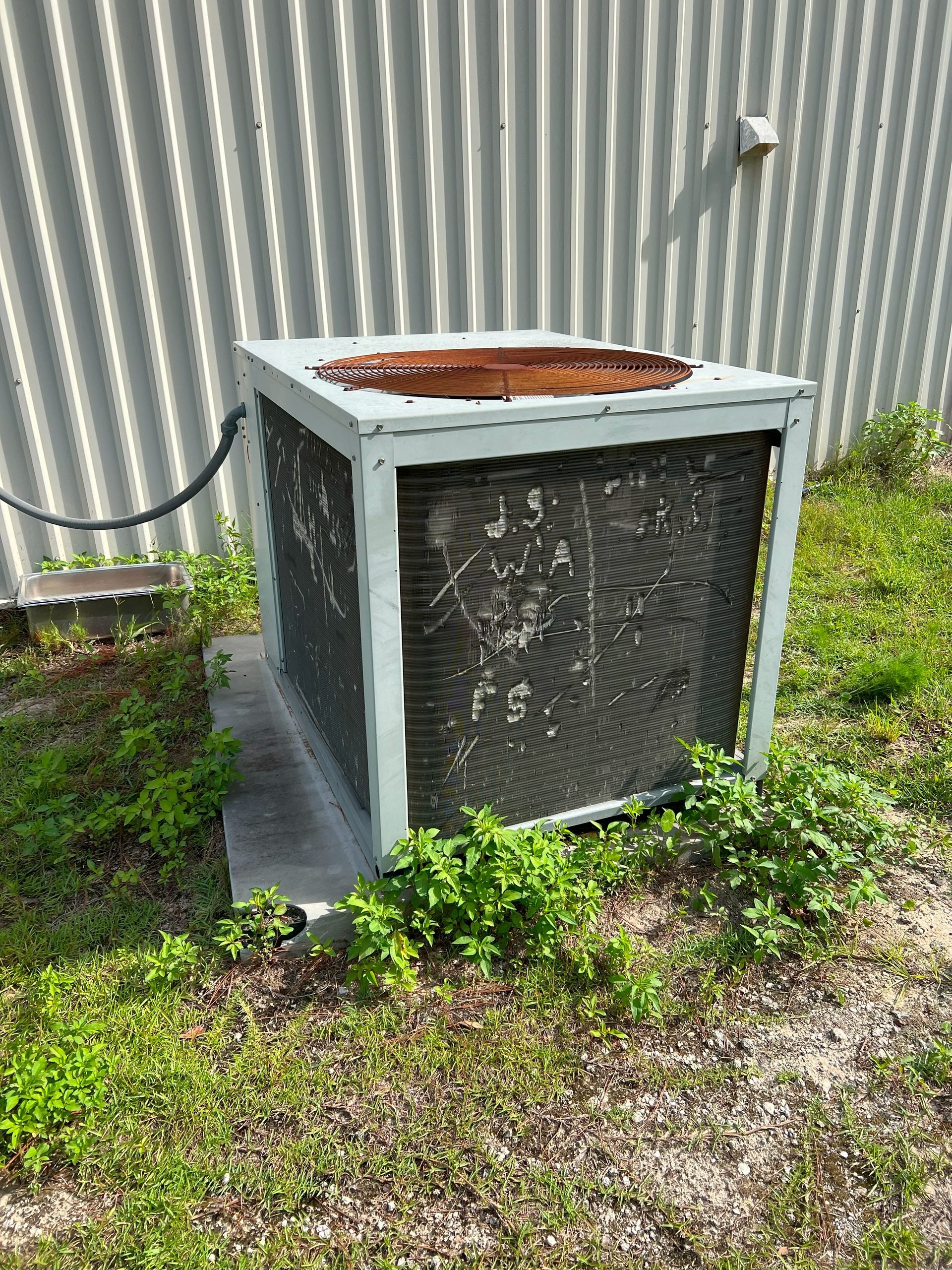 An old air conditioner is sitting in the grass in front of a building.