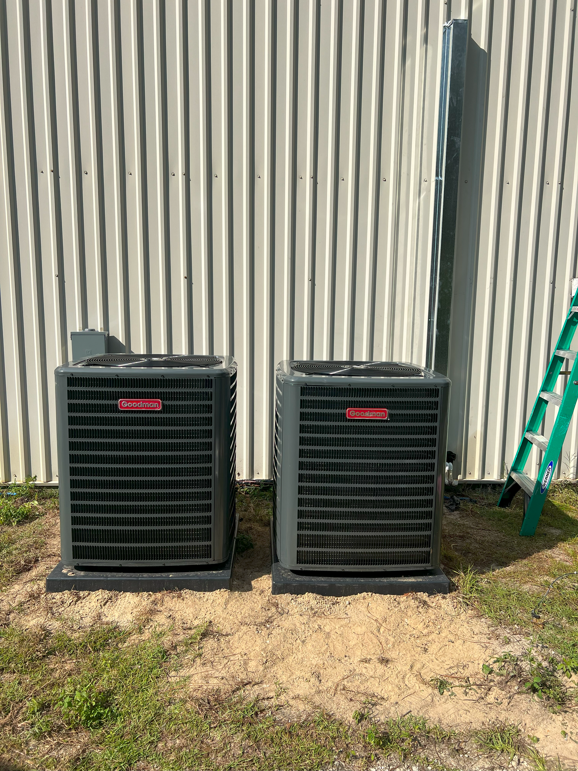 Two air conditioners are sitting next to each other in front of a building.
