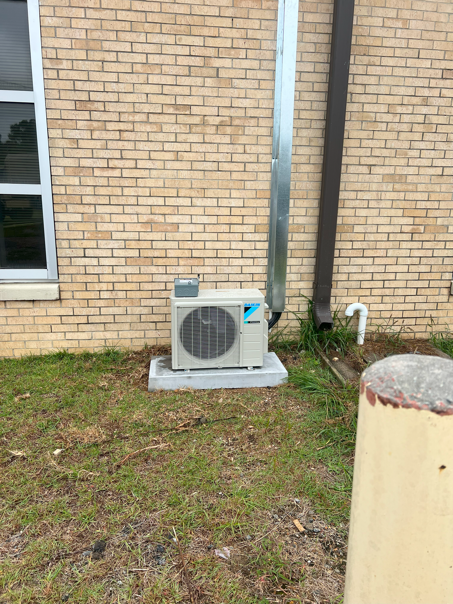 A small air conditioner is sitting on the side of a brick building.