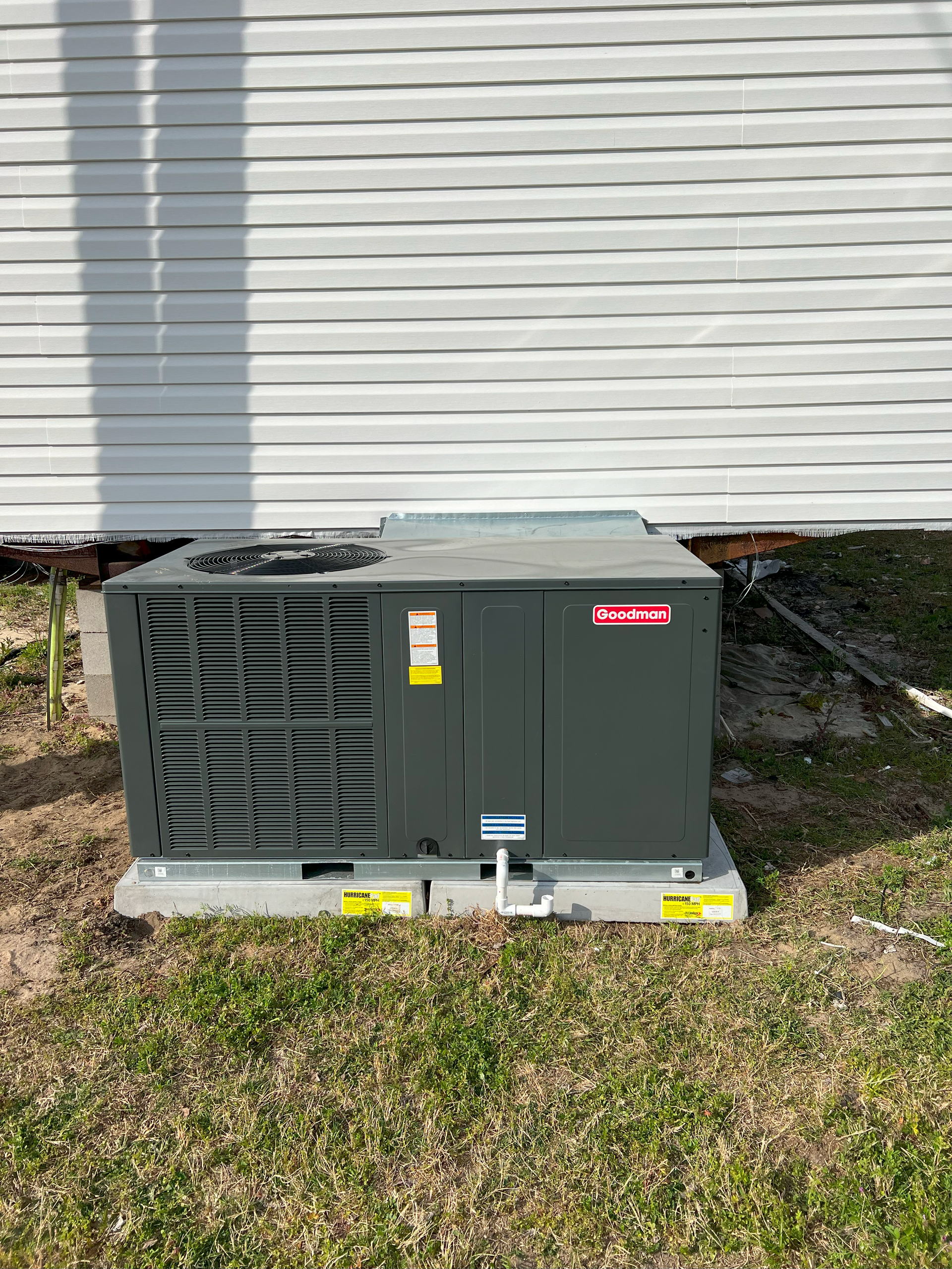 An air conditioner is sitting in the grass in front of a house.