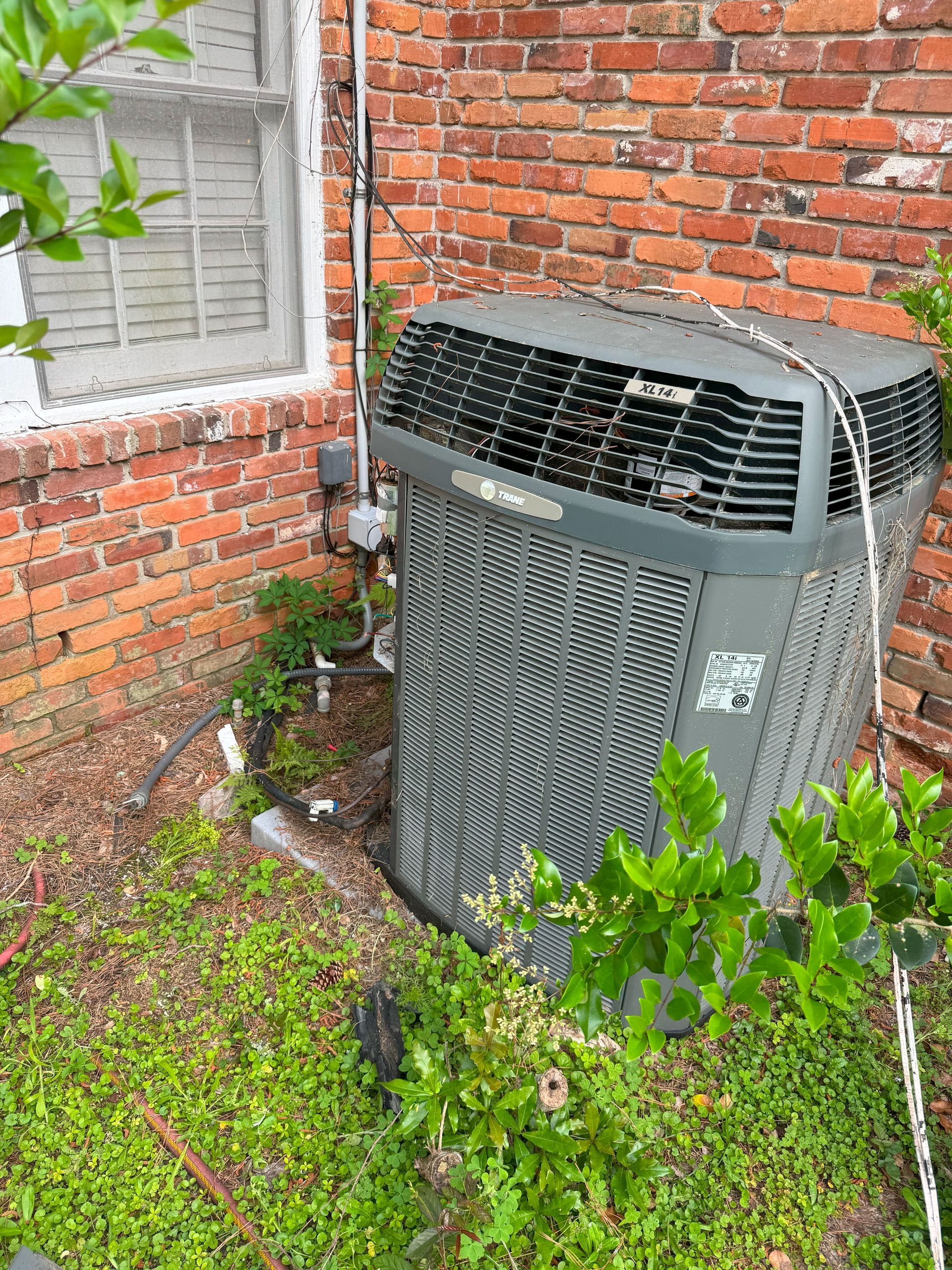 An air conditioner is sitting on the side of a brick building.